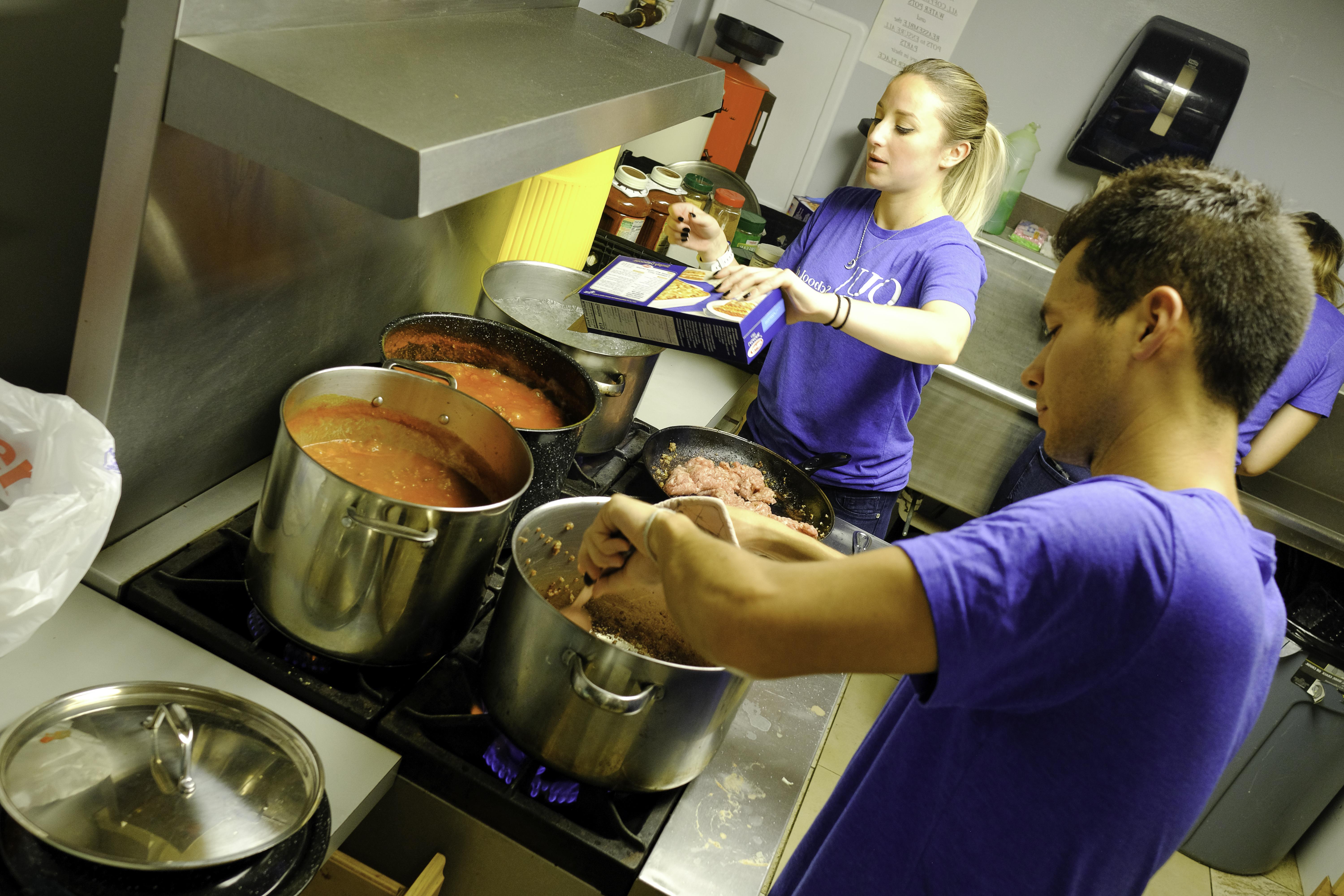 Two medical students stand by stove cooking meat and pasta for lasagna.